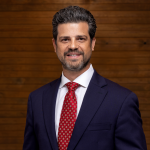 Smiling man in a suit with a red tie against a wooden background