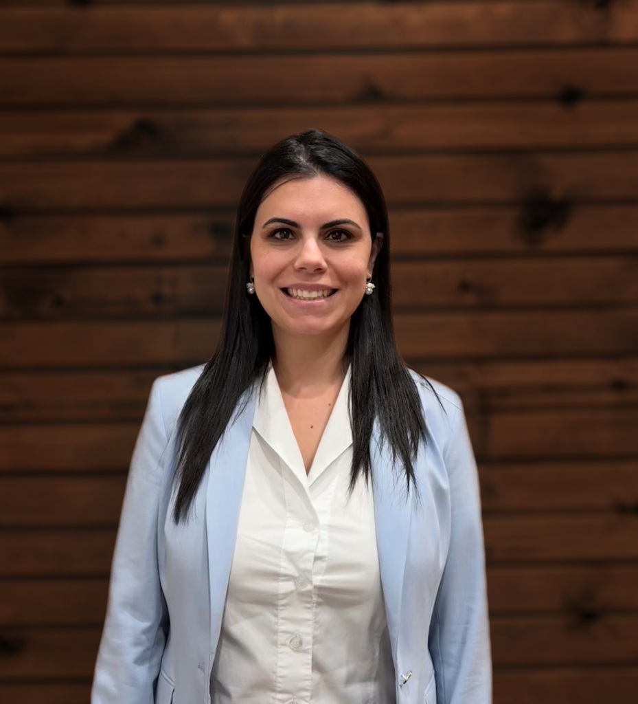 Woman in light blue blazer smiles against wooden wall background