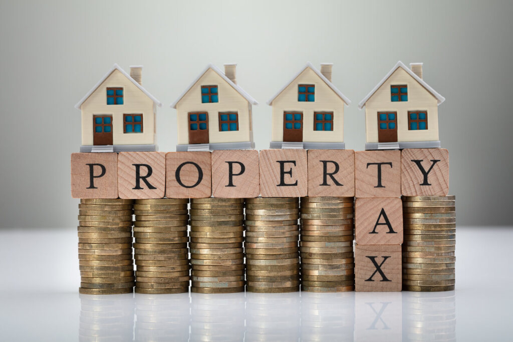 Miniature houses on stacked coins with property tax text blocks.