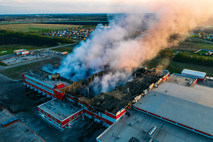Aerial view of large warehouse fire with smoke rising.