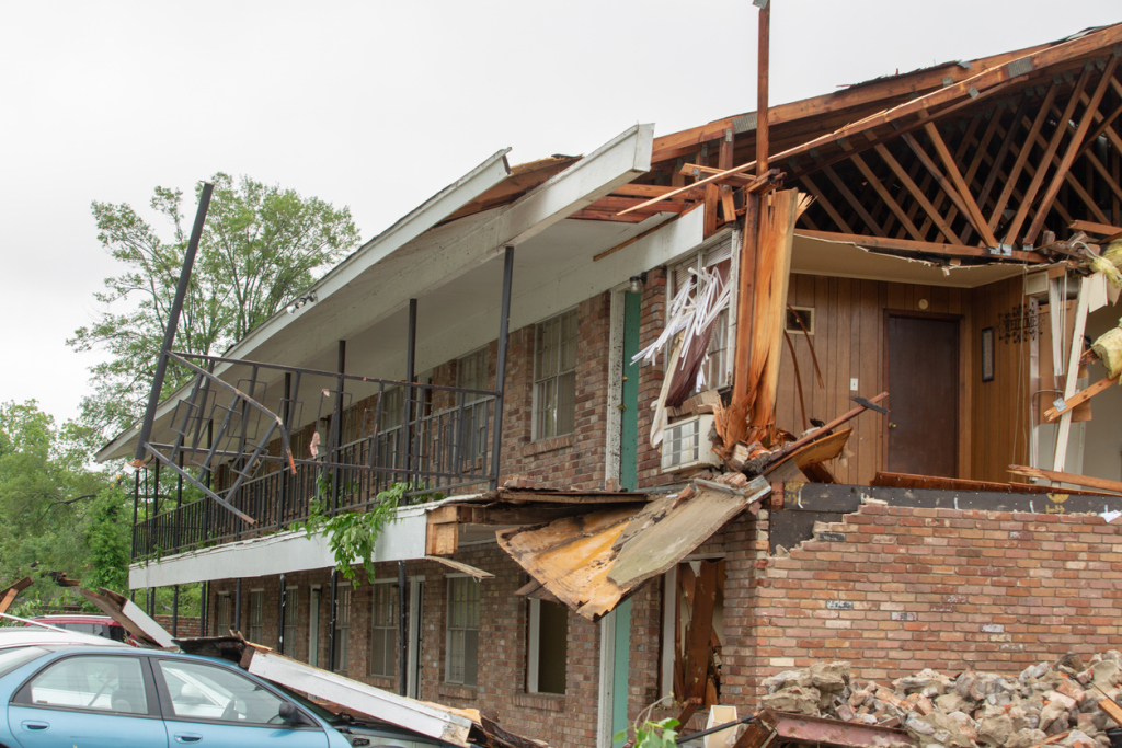 Damaged apartment building post-storm with debris and broken structure.