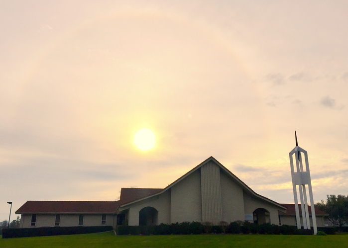 Church building with a sun halo in the sky, featuring a white tower.