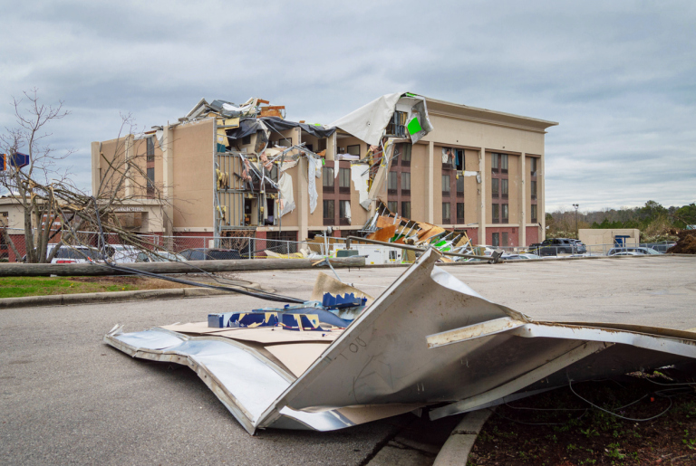 Damaged hotel building after severe storm with debris on ground.