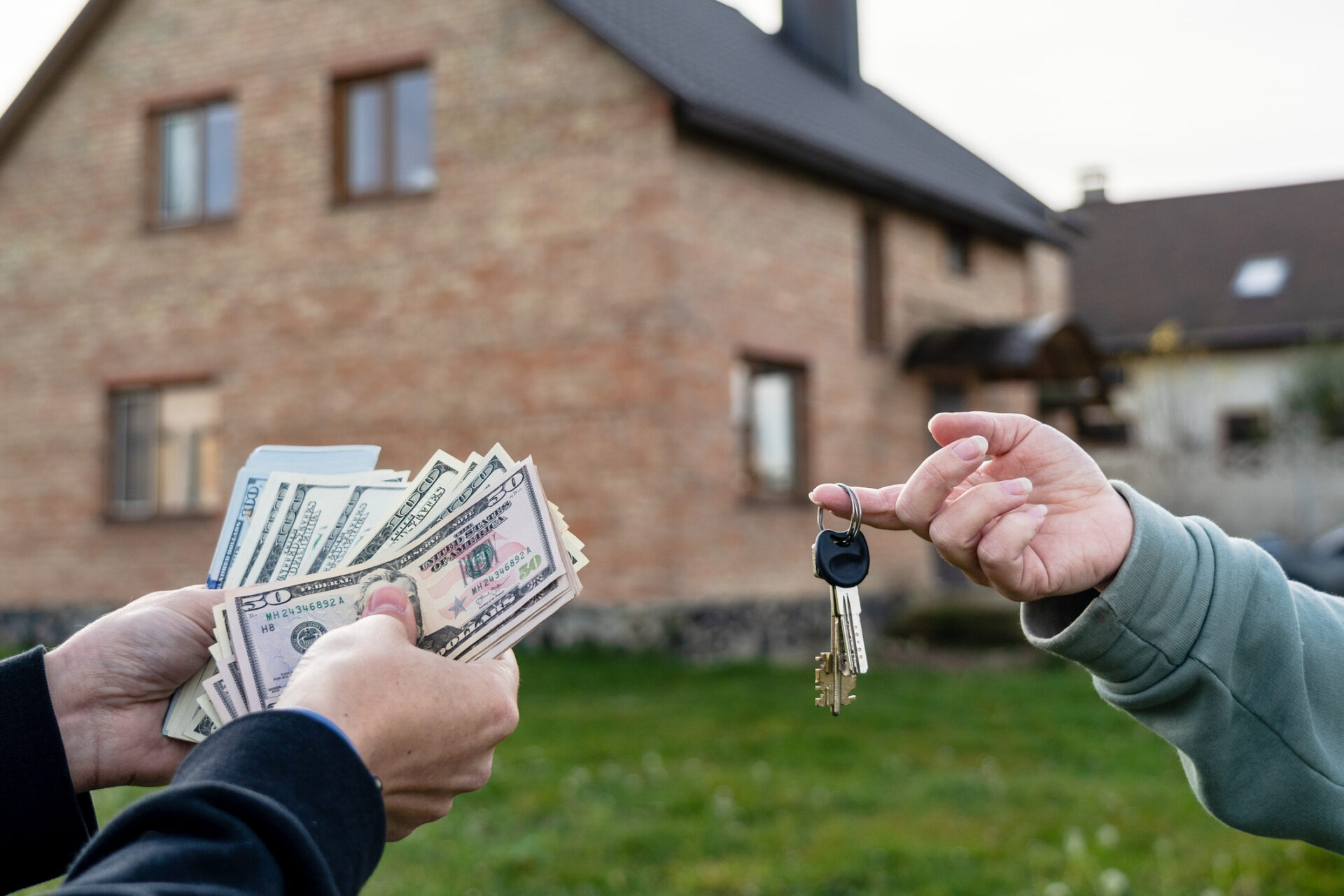 Person exchanging money and house keys in front of a new home