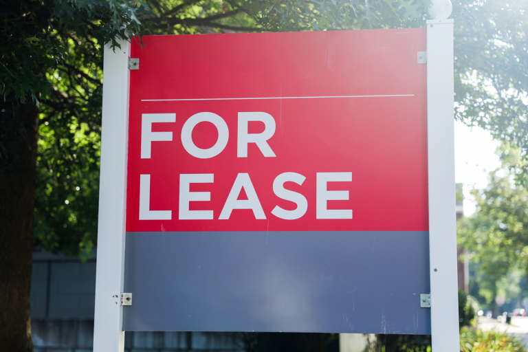 Red 'For Lease' sign in sunlight against tree background