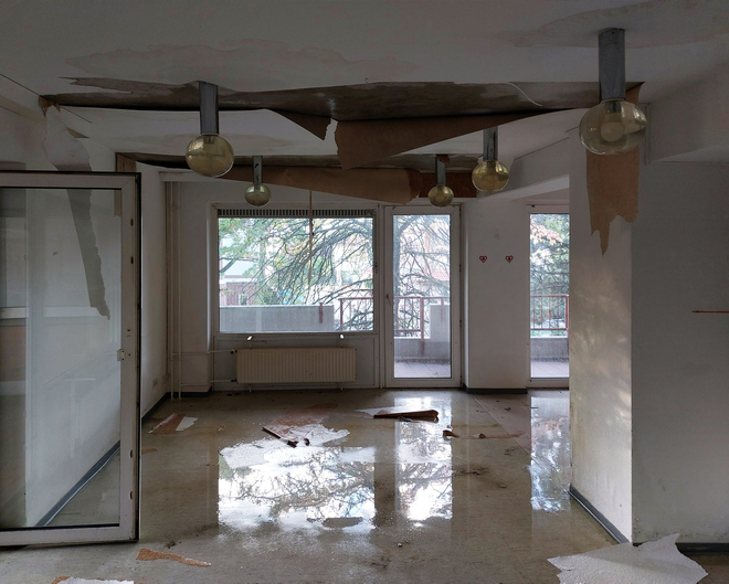 Abandoned, water-damaged room with peeling ceiling and broken floor tiles.