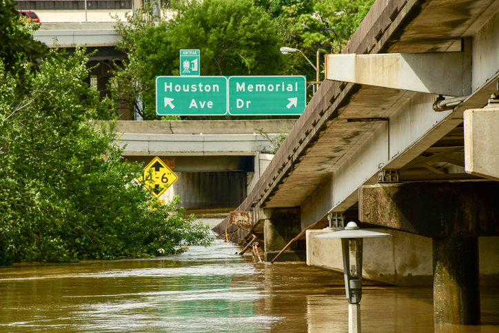 Flooded street under a highway overpass with Houston Ave signs.