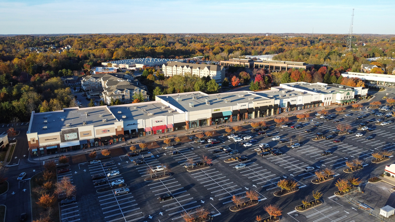 Aerial view of a shopping center and parking lot surrounded by trees.
