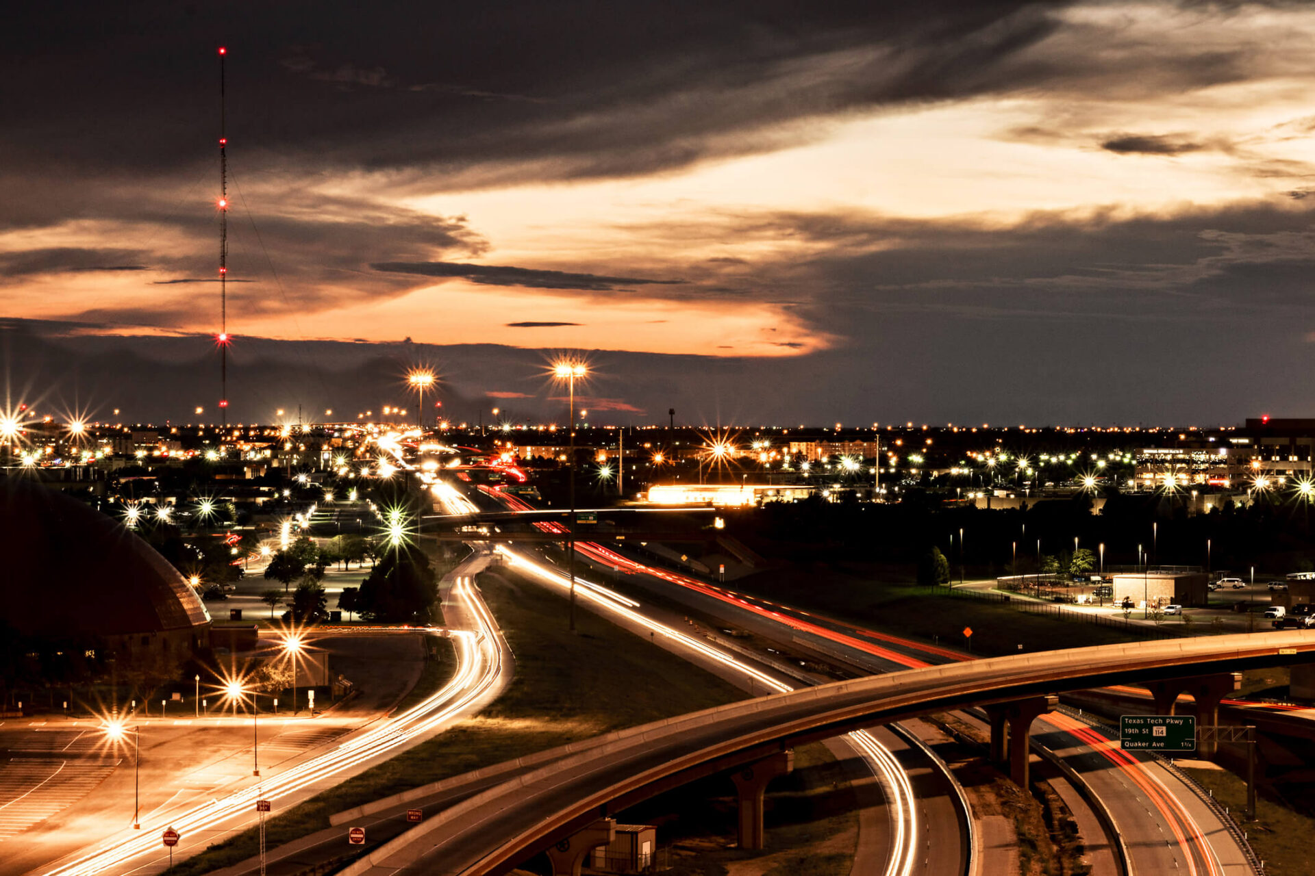 Aerial view of a bustling highway junction at sunset with city lights.