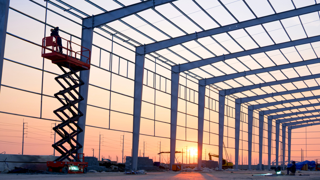 Construction worker on lift in steel building frame at sunset
