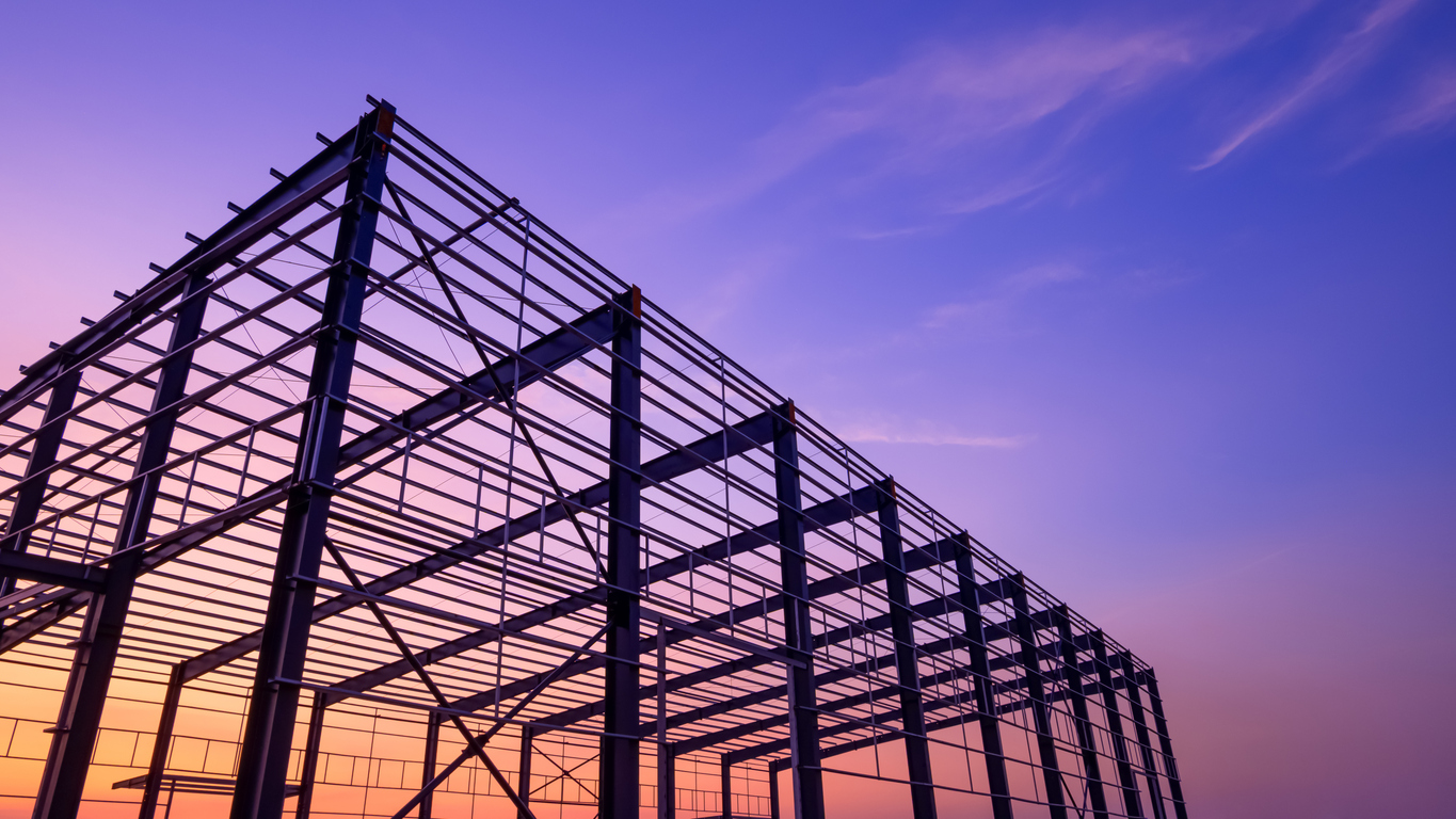 Steel building framework against a vibrant sunset sky