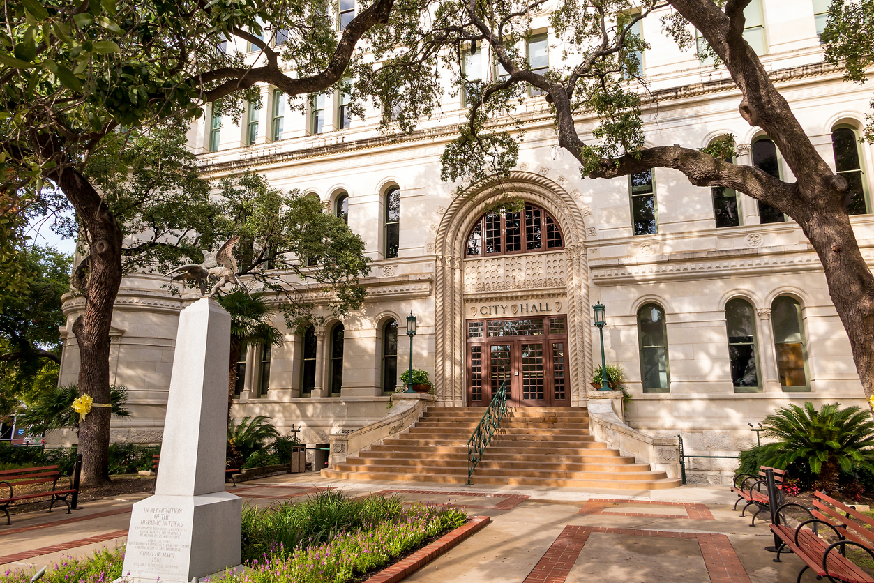 Historic city hall building with trees and statue in foreground.
