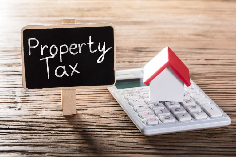 Mini house on calculator next to property tax sign on table